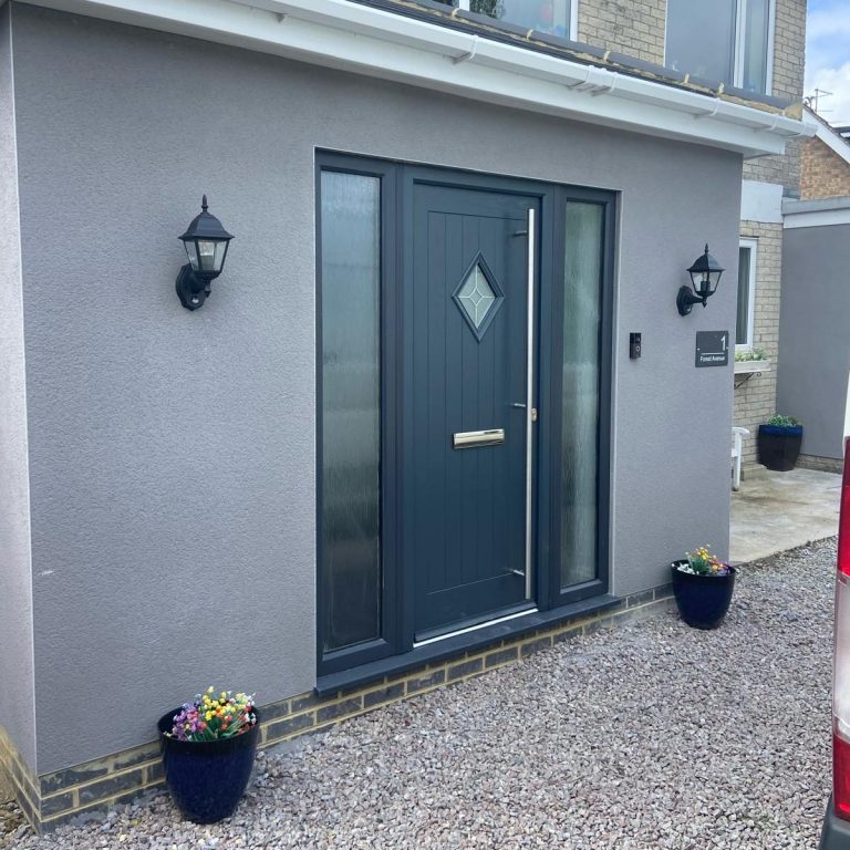 Modern grey front door with diamond-shaped window and potted plants on either side.