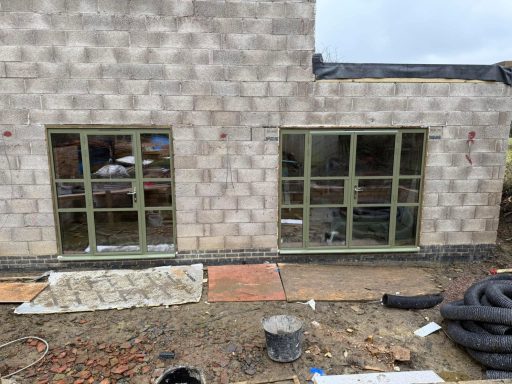 Two green-framed windows on a newly constructed brick wall.