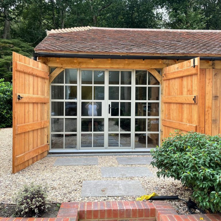 Wooden building with glass-fronted doors, surrounded by gravel and greenery.