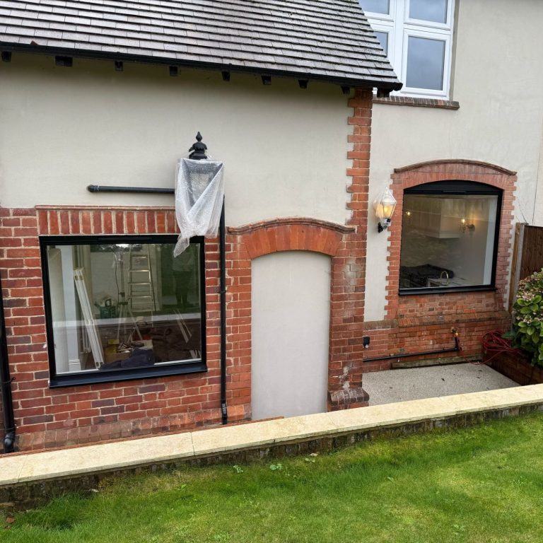 A brick house exterior with a door, windows, and a garden area.