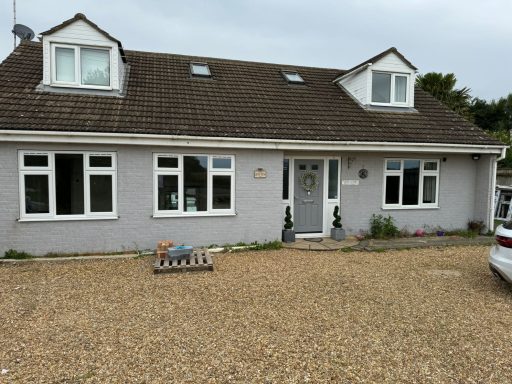 A grey bungalow with multiple windows and a gravel driveway.