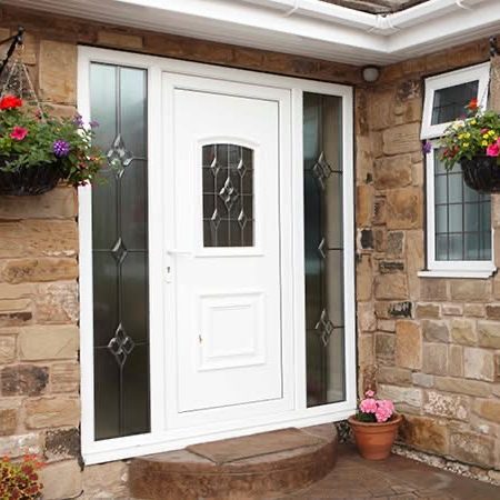 White front door with glass panels, flanked by flower baskets and stone wall.