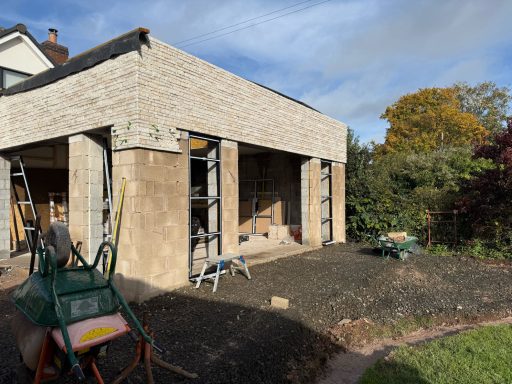 Construction site with scaffolding and newly plastered walls, surrounded by trees.