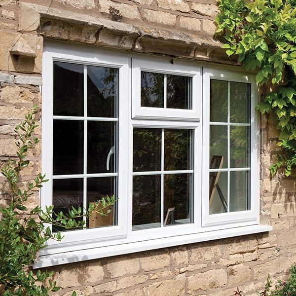 White window with multiple panes, set in a stone wall, surrounded by greenery.