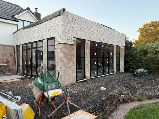 Newly constructed extension with large windows, gravel pathway, and construction equipment nearby.